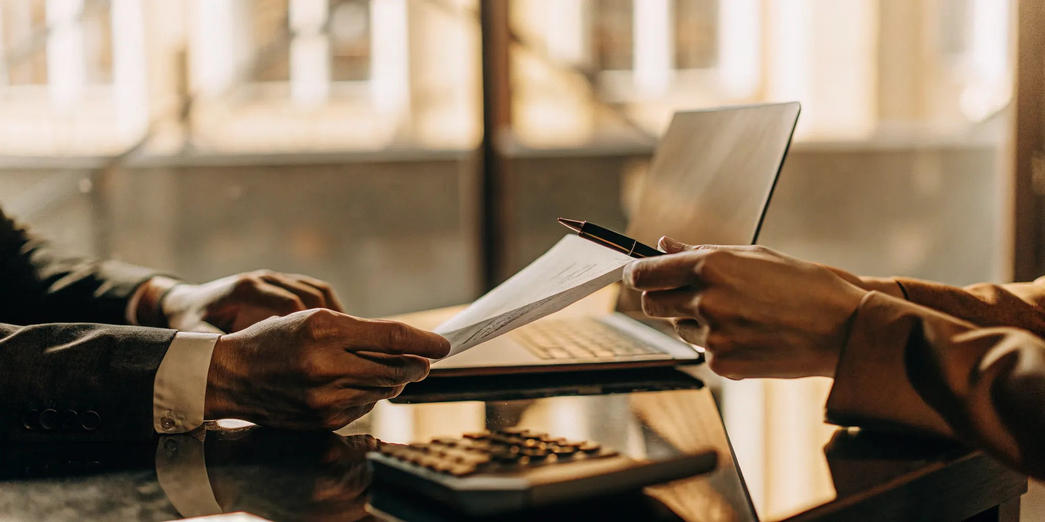 A professional business desk with hands holding an official IRS tax notice, calculator, and laptop